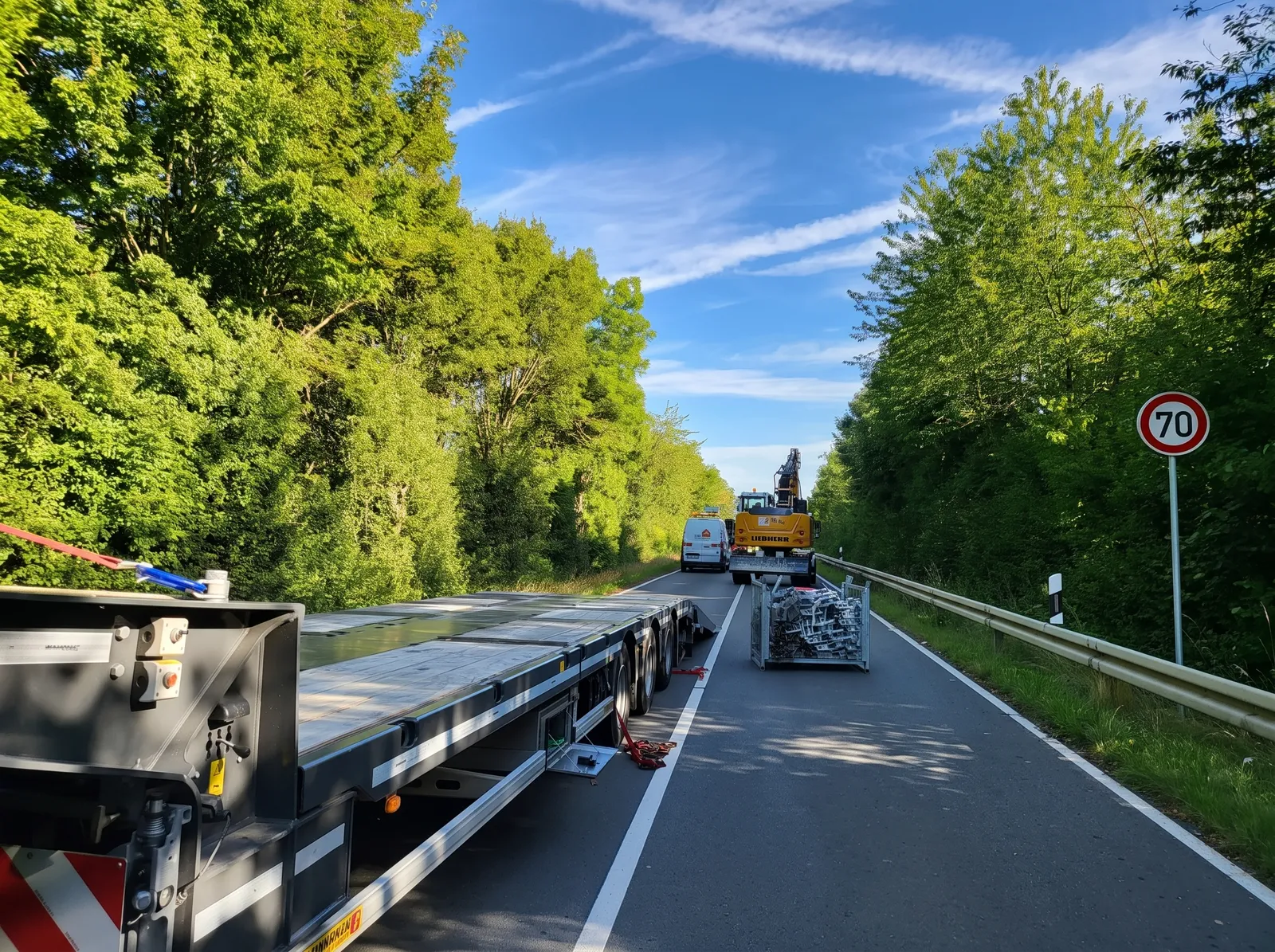 Baustellenlogistik mit Tieflader und Liebherr-Bagger auf der Zufahrtsstraße