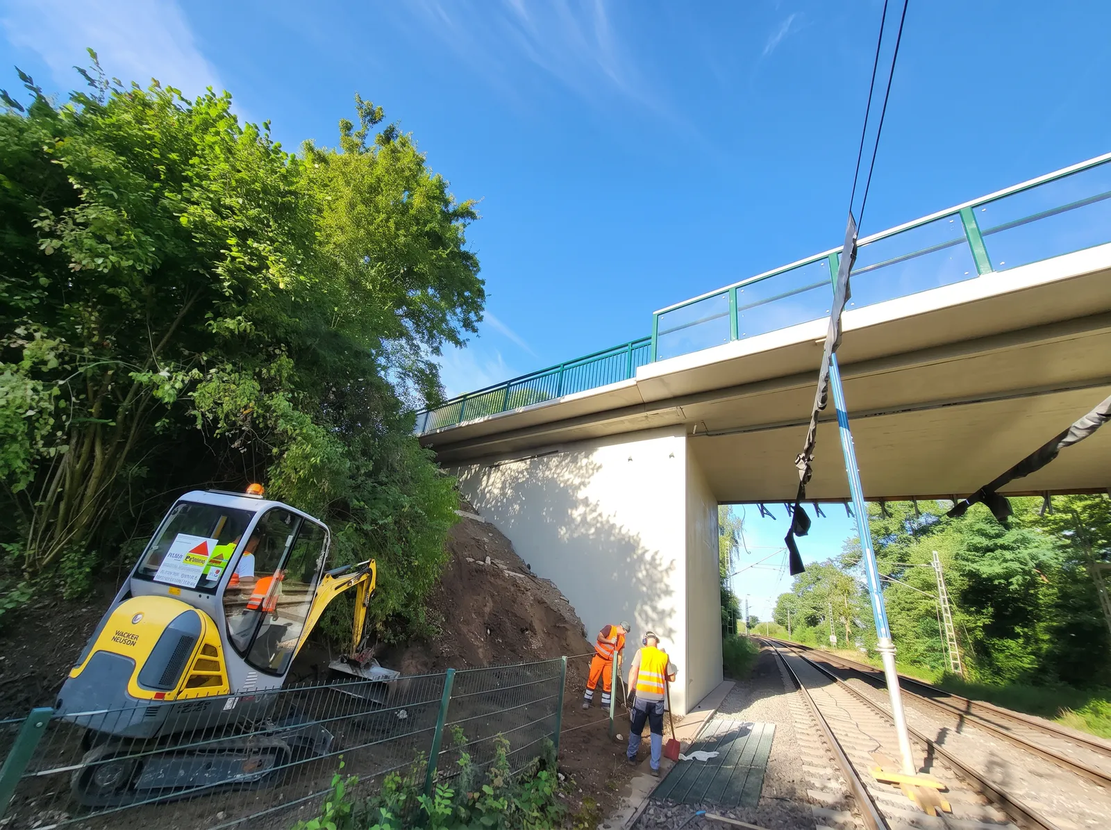 Arbeiten an der Brücke über der Bahnstrecke mit Minibagger am Bahndamm